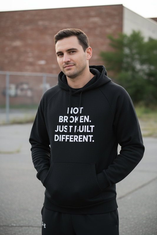 Man outdoors wearing Not Broken Just Built Different black Under Armour hoodie